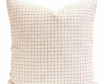 May include: A square throw pillow featuring a light beige fabric base with a dark navy blue grid pattern. The textile has a visible woven texture, and the pillow is plumped to create a soft, rounded shape with defined corners and edges.