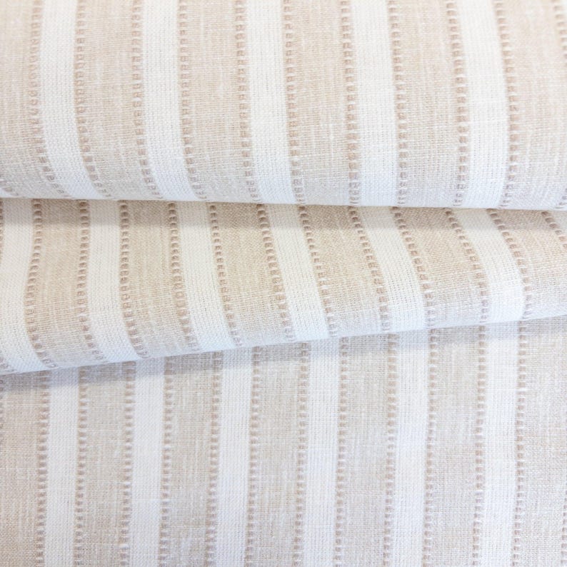 May include: A textile fabric featuring a repeating pattern of vertical stripes in alternating shades of beige and white. The design includes thin, textured, dotted lines running parallel to the wider solid stripes, creating a consistent linear visual.