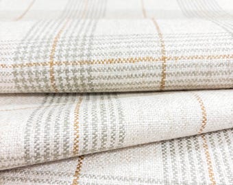 May include: Close-up of folded fabric with a plaid pattern. The fabric is primarily off-white with a gray and gold plaid design. The texture of the fabric is visible, with a woven appearance. The fabric is folded over itself, showing multiple layers.