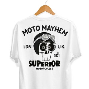 Peut inclure: T-shirt blanc avec un motif noir d'un crâne portant un casque et des lunettes. Le texte "MOTO MAYHEM" est au-dessus du crâne, et le texte "SUPERIOR MOTORCYCLES" est en dessous du crâne. Le texte "LDN" et "U.K." sont de chaque côté du crâne, et le texte "EST 2021" est en dessous du crâne.