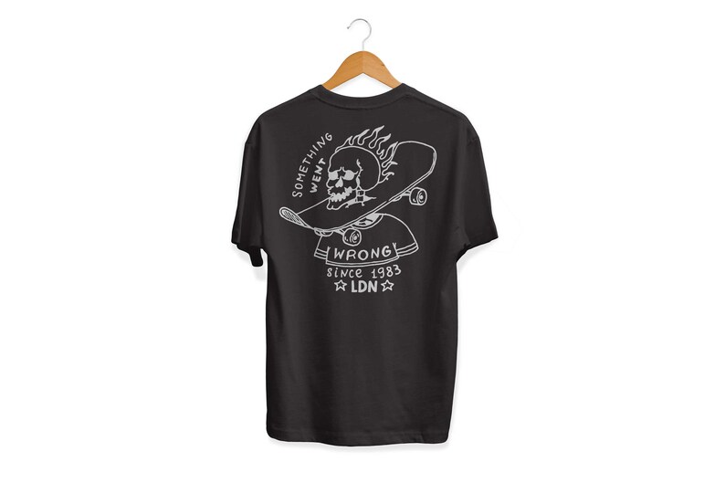 K&ouml;nnte beinhalten: Schwarzes T-Shirt mit einem wei&szlig;en Grafikdruck eines Sch&auml;dels, der ein Skateboard mit Flammen tr&auml;gt. Der Text "Something Went Wrong" und "Since 1983 LDN" ist unter dem Grafikdruck aufgedruckt.