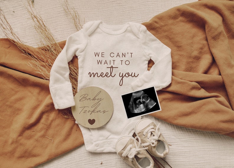 K&ouml;nnte beinhalten: Ein wei&szlig;er Strampler mit dem Text "We can't wait to meet you". Ein Holz-Kreis mit dem Text "Baby [name]" und einem Herz. Ein Schwarzwei&szlig;-Ultraschallbild. Ein Paar wei&szlig;e Babyschuhe.