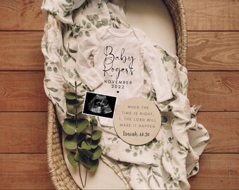 Könnte beinhalten: Ein weißer Baby-Strampler mit dem Text "Baby Rogers November 2022" in schwarzer Schrift. Neben dem Strampler befindet sich ein Schwarzweiß-Ultraschallbild. Ein rundes Holzschild mit dem Text "When the time is right, I, the Lord will make it happen Isaiah 60.20" befindet sich in der rechten unteren Ecke des Bildes.