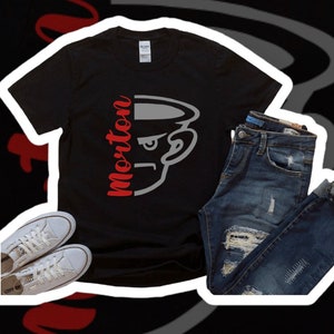 May include: Black t-shirt featuring a red and grey graphic of a cartoon face with the word "Morton" printed on the left side of the face. The t-shirt is styled with blue jeans and white trainers.