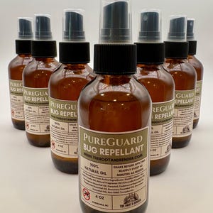 May include: A collection of amber-colored glass spray bottles of PureGuard Bug Repellant. Each bottle has a black cap and a clear plastic spray nozzle. The label indicates the product is made with 100% natural oil and lists active ingredients. The bottles are 4 oz.