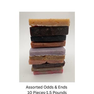 May include: A stack of ten rectangular soap bars in various colors including tan, dark brown, black, lavender, and pink. The text below the stack reads Assorted Odds & Ends 10 Pieces-1.5 Pounds, indicating the total weight of the soap collection.