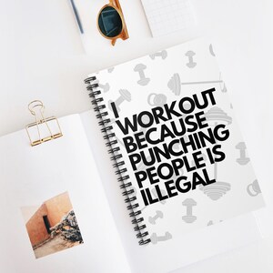 以下が含まれることがあります： 「I WORKOUT BECAUSE PUNCHING PEOPLE IS ILLEGAL」の黒い文字が入った白いリング綴じノート。ノートには灰色のダンベルのパターンがあります。白い表面には、サングラスと金のペーパークリップも含まれています。