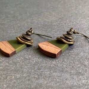 May include: A pair of earrings with a green and brown wood design and a brass charm. The earrings have a simple hook closure.