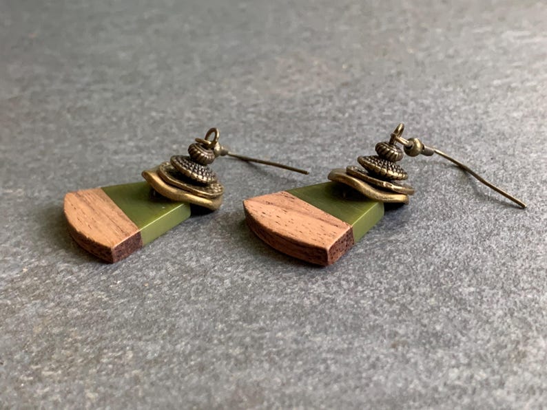 May include: A pair of earrings with a green and brown wood design and a brass charm. The earrings have a simple hook closure.