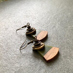 May include: A pair of earrings with a green and brown wood design. The earrings feature a gold-toned metal charm with a layered design.