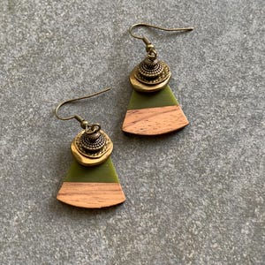 May include: A pair of green and brown wood earrings with a brass accent. The earrings are shaped like a fan and have a brass charm in the center.