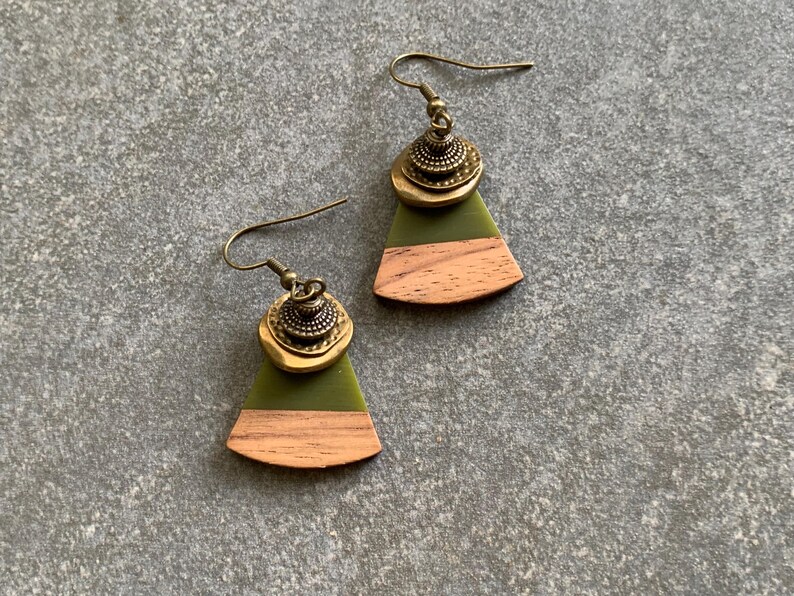 May include: A pair of green and brown wood earrings with a brass accent. The earrings are shaped like a fan and have a brass charm in the center.