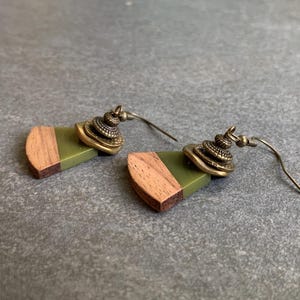 May include: A pair of earrings with green and brown wood accents and gold-toned metal accents. The earrings have a geometric shape and are suspended from a wire.