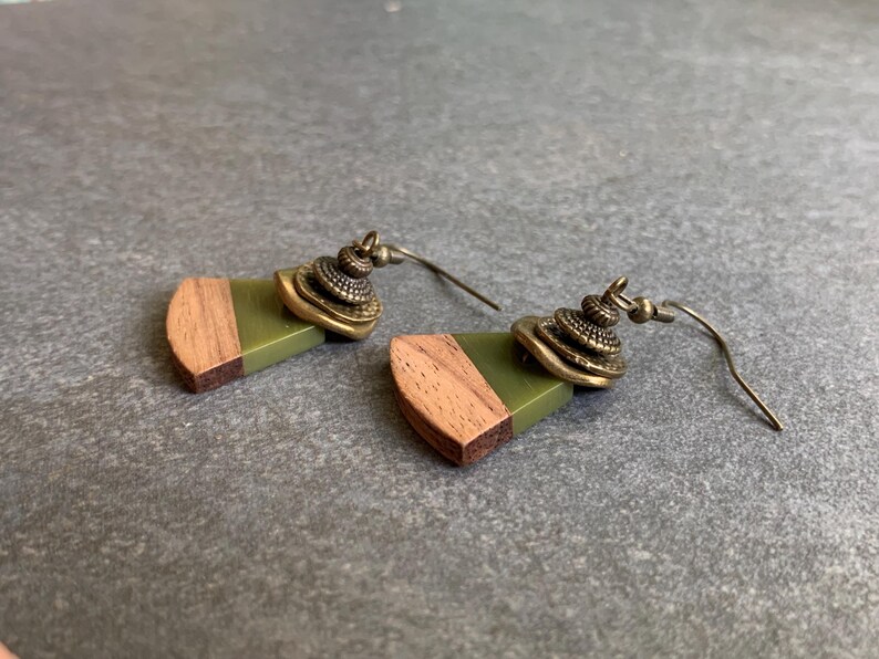 May include: A pair of earrings with green and brown wood accents and gold-toned metal accents. The earrings have a geometric shape and are suspended from a wire.