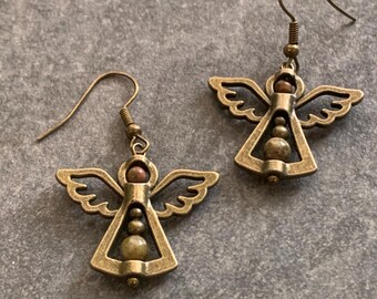 May include: A pair of antique bronze-colored angel earrings. Each earring features an angel silhouette with outstretched wings and a beaded body. The earrings have a hook closure.