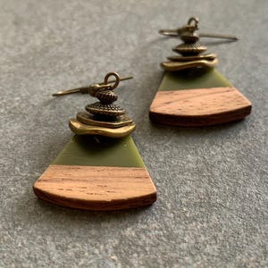 May include: A pair of green and brown wood earrings with gold metal accents. The earrings are shaped like a triangle with a rounded edge.