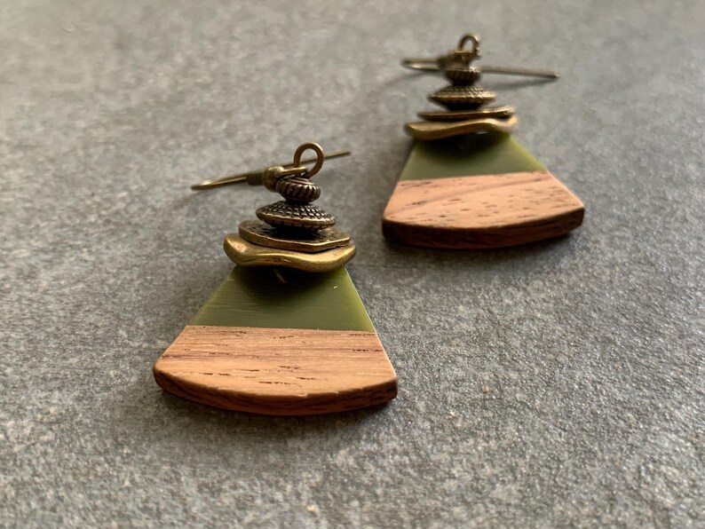 May include: A pair of green and brown wood earrings with gold metal accents. The earrings are shaped like a triangle with a rounded edge.