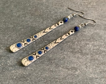 May include: Silver dangle earrings with a hammered texture and blue lapis lazuli beads. The earrings feature a geometric pattern with small circles.