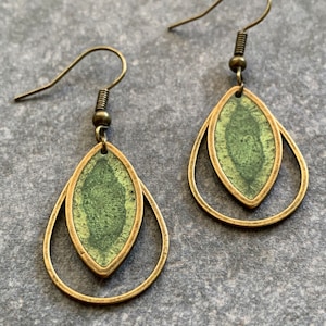 Könnte beinhalten: Ein Paar grüne und goldene Ohrringe mit Tropfenform. Die Ohrringe haben ein zweilagiges Design mit einem kleineren grünen Tropfen innerhalb eines größeren goldenen Tropfens.