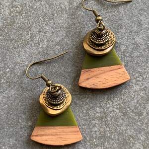 May include: A pair of green and brown wood earrings with a gold metal accent. The earrings are shaped like a triangle with a rounded top.