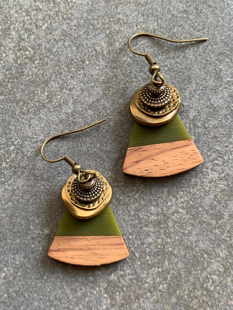 May include: A pair of green and brown wood earrings with a gold metal accent. The earrings are shaped like a triangle with a rounded top.