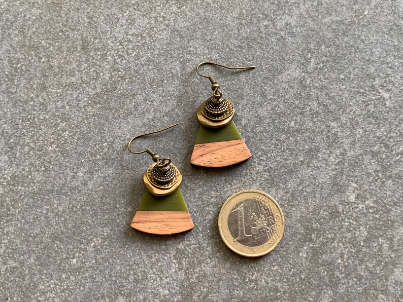 May include: A pair of green and brown wood earrings with gold accents. The earrings are shaped like a triangle with a rounded bottom.