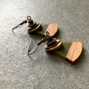 May include: A pair of earrings with green and brown wooden accents. The earrings feature a layered, gold-toned metal design.