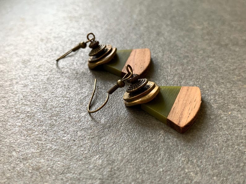 May include: A pair of earrings with green and brown wooden accents. The earrings feature a layered, gold-toned metal design.