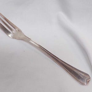 May include: A silver fork with a slightly bent tine. The fork has a simple design with a slightly curved handle.