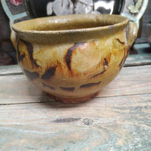May include: A large, brown ceramic bowl with a wide rim and two handles. The bowl has a mottled glaze with brown and yellow accents.