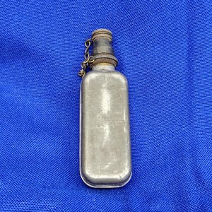 Peut inclure: Petite flasque métallique rectangulaire avec un bouchon à vis et une chaîne. La flasque a une finition argentée avec des signes d'usure. Le bouchon est foncé avec un anneau de couleur laiton. Sur fond bleu.