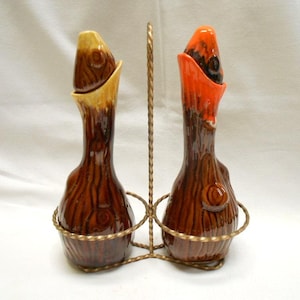 Può includere: Un set vintage di saliera e pepiera. Gli shaker in ceramica hanno un design a tronco d'albero con toni marroni, arancioni e gialli. Sono in un supporto in metallo color oro. Il set è un oggetto decorativo per la cucina.