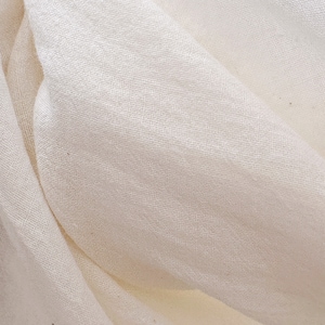 May include: Close-up of a white fabric with a smooth, woven texture. The fabric is folded and draped, creating soft folds and wrinkles.