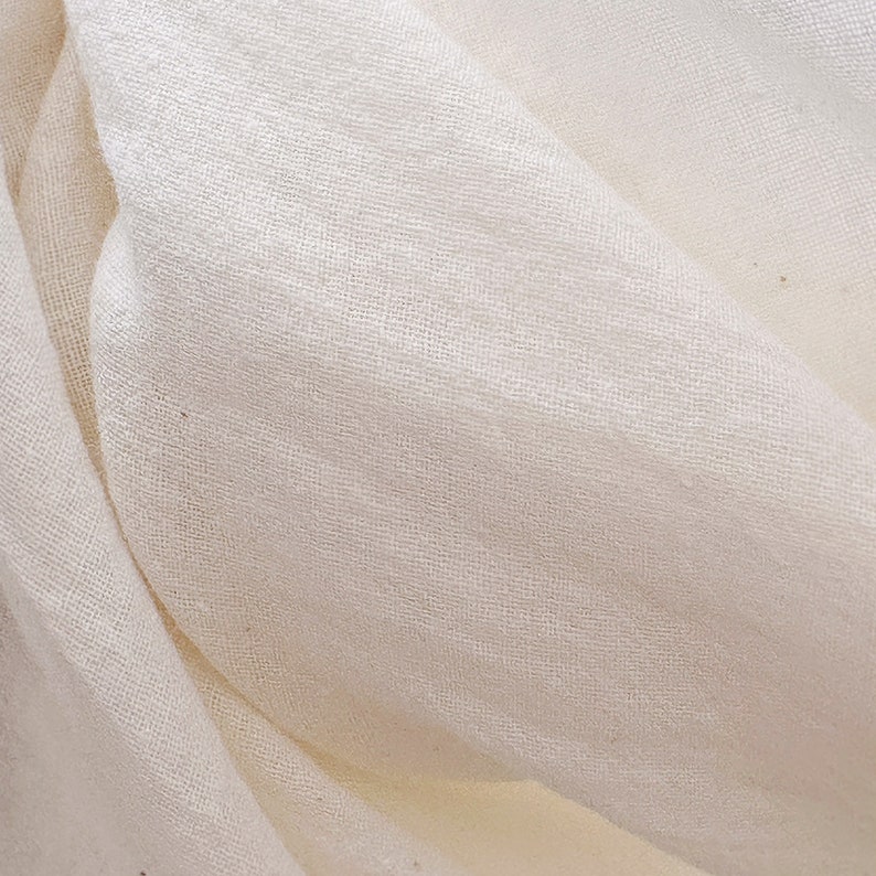 May include: Close-up of a white fabric with a smooth, woven texture. The fabric is folded and draped, creating soft folds and wrinkles.