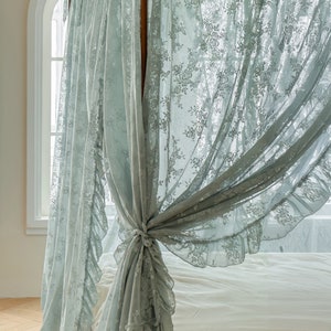 May include: A light blue lace canopy bed curtain with a ruffled edge. The curtain is tied back with a bow.