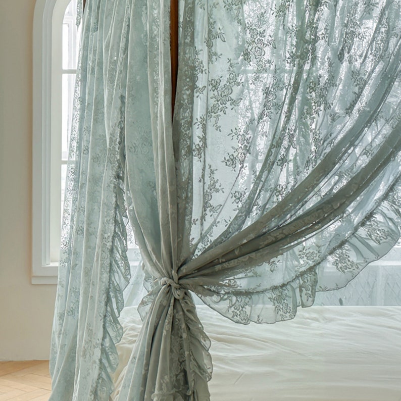 May include: A light blue lace canopy bed curtain with a ruffled edge. The curtain is tied back with a bow.
