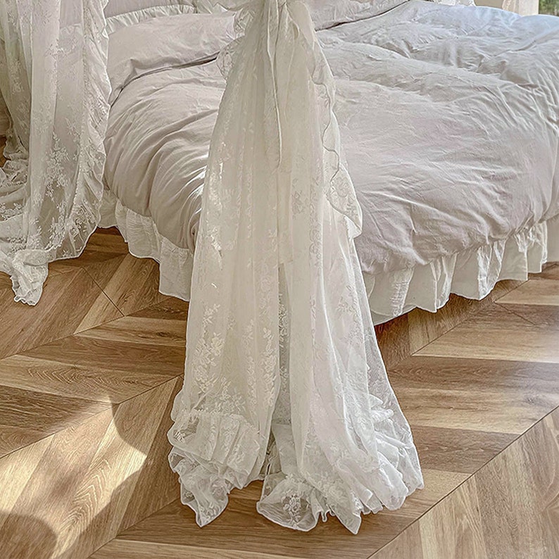 May include: White lace canopy bed with a white ruffled bed skirt and a white duvet cover. The bed is on a wooden floor with a herringbone pattern.