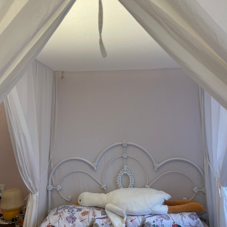 May include: White canopy bed with a white metal frame and a white plush goose-shaped pillow on the bed.