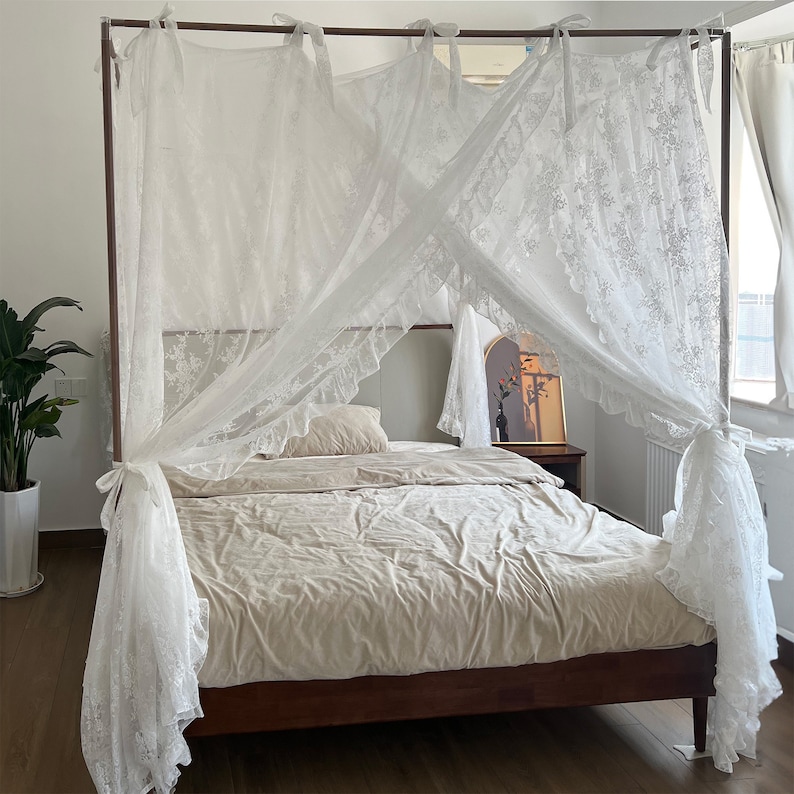 May include: White lace canopy bed frame with a beige duvet and pillows. The canopy is draped over the bed frame and has a ruffled edge.