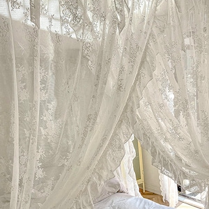 May include: White lace curtains with a ruffled edge, draped over a bed with white bedding. The curtains are sheer and delicate, creating a romantic and airy atmosphere.