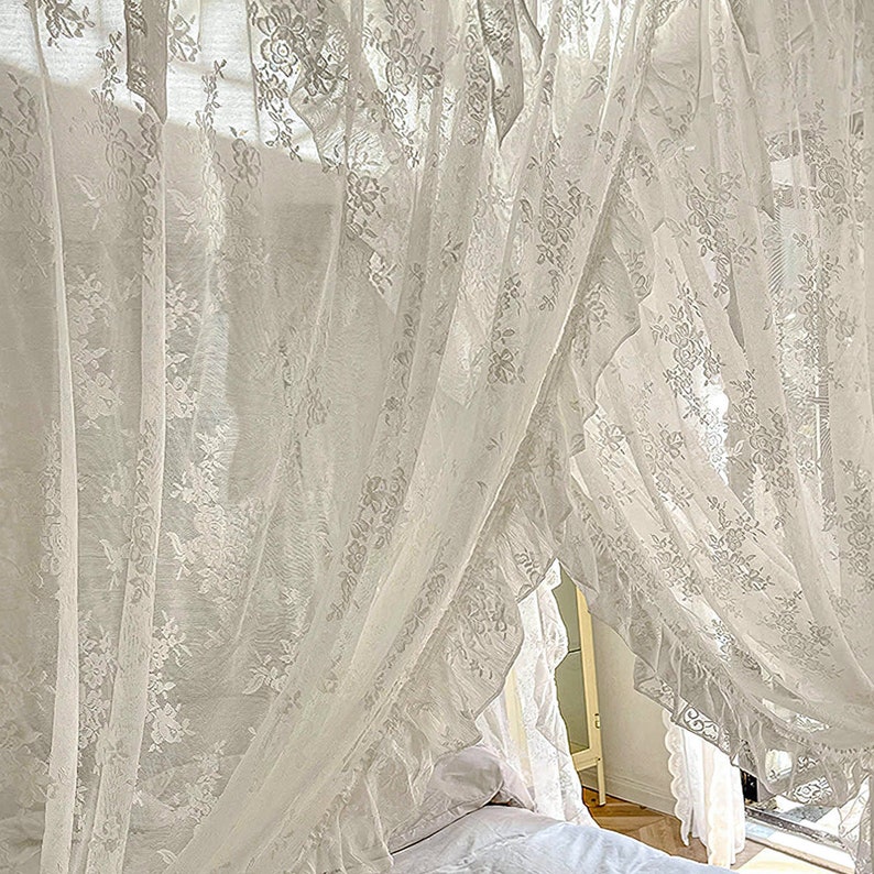 May include: White lace curtains with a ruffled edge, draped over a bed with white bedding. The curtains are sheer and delicate, creating a romantic and airy atmosphere.