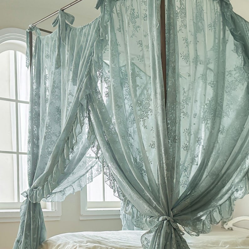 May include: A light blue lace canopy bed curtain with ruffles. The curtain is draped over a bed frame and is tied back on each side.