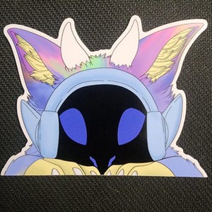 May include: A sticker featuring a stylized, anthropomorphic creature with a black face, blue eyes, and light blue headphones. The creature has large, colorful ears with shades of purple, yellow, and pink. The sticker is on a black background.