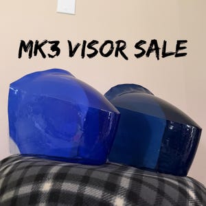 May include: Two MK3 visors, one in a bright royal blue and the other in a deep navy blue, both featuring a smooth, curved, and semi-transparent finish. The text MK3 VISOR SALE is displayed in black capital letters above the two curved visors.