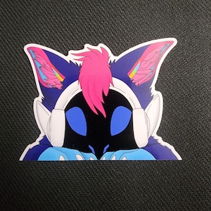 May include: A sticker featuring a stylized cat-like character with blue and purple fur, large blue eyes, and a black face. The character wears white headphones and has a pink mohawk. The ears have pink and blue accents.
