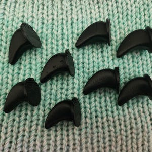 Può includere: Otto artigli di plastica neri, che ricordano gli artigli degli animali, sono disposti su una superficie di maglia verde.