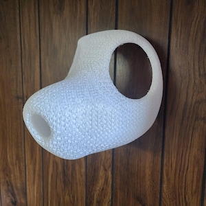 May include: A white, 3D printed, abstract sculpture with a textured surface and a large hole in the center. The sculpture is mounted on a wooden wall.