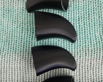 May include: Four black plastic fin-shaped objects, possibly for a costume or prop, arranged vertically on a light blue and white knitted surface.
