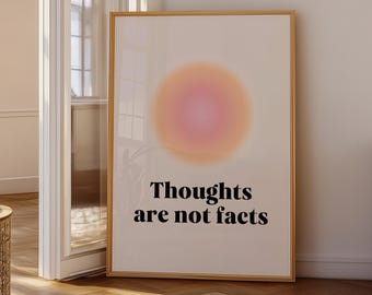 May include: A framed art print with a soft, gradient design in shades of orange and pink. The text "Thoughts are not facts" is printed in black. The artwork is displayed in a room with a wooden floor and a door.