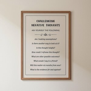 May include: A framed wall art print featuring the text CHALLENGING NEGATIVE THOUGHTS and ASK YOURSELF THE FOLLOWING, followed by a list of eight reflective questions in black font on a light background, enclosed in a simple wooden frame.